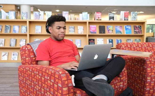 在图书馆里，一个男生坐在椅子上摆弄他的笔记本电脑